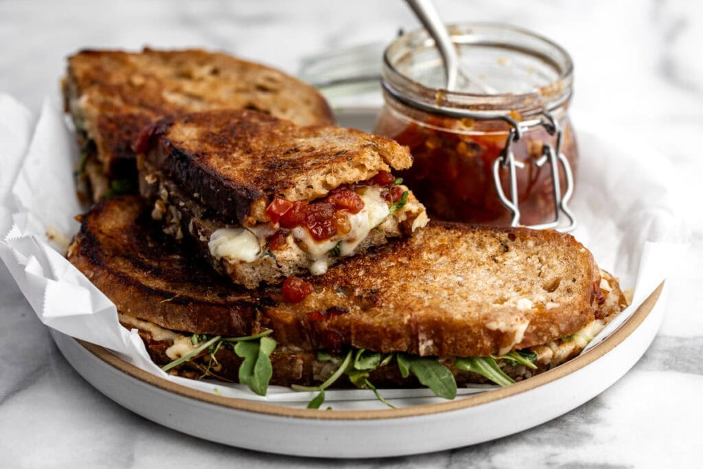 grilled cheese with tomato bacon jam and arugula on plate.