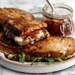 grilled cheese with tomato bacon jam and arugula on plate.