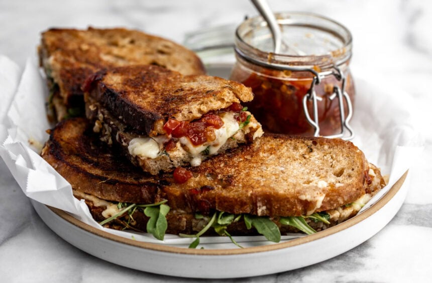 grilled cheese with tomato bacon jam and arugula on plate.