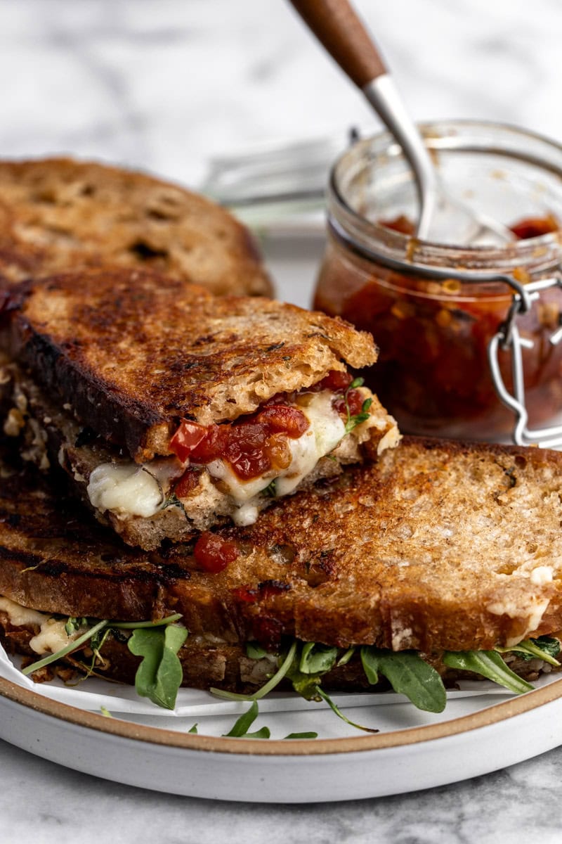 sourdough grilled cheese with tomato bacon jam with arugula cut in half.