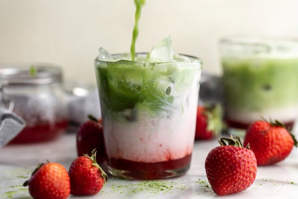 Iced Strawberry Matcha Latte in glass surrounded by strawberries.