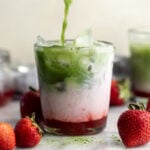 Iced Strawberry Matcha Latte in glass surrounded by strawberries.