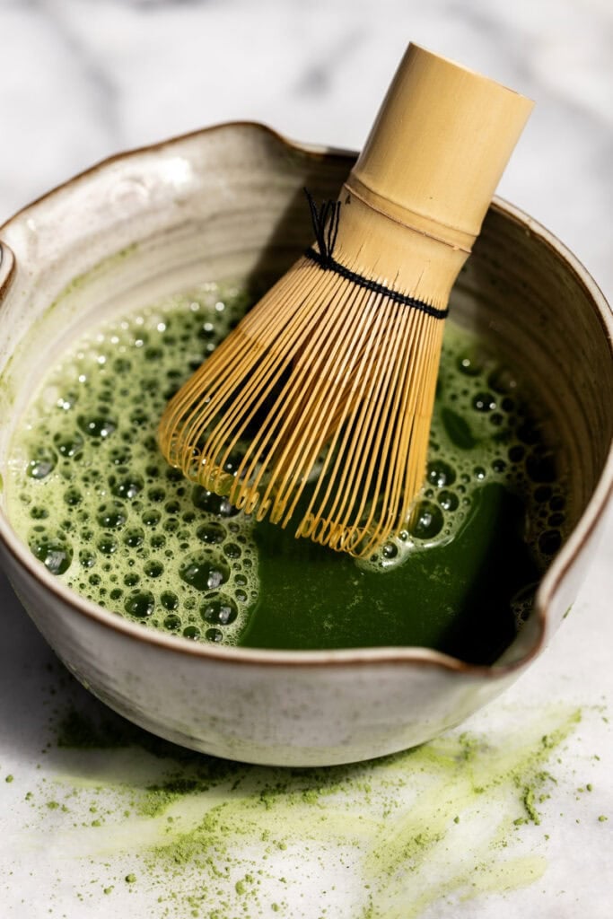 whisked matcha tea in bowl with bamboo whisk.