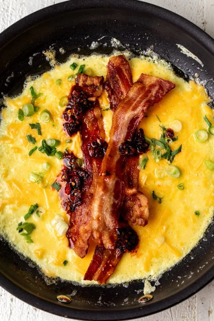 cooked eggs in pan with cheese bacon and chili crisp.