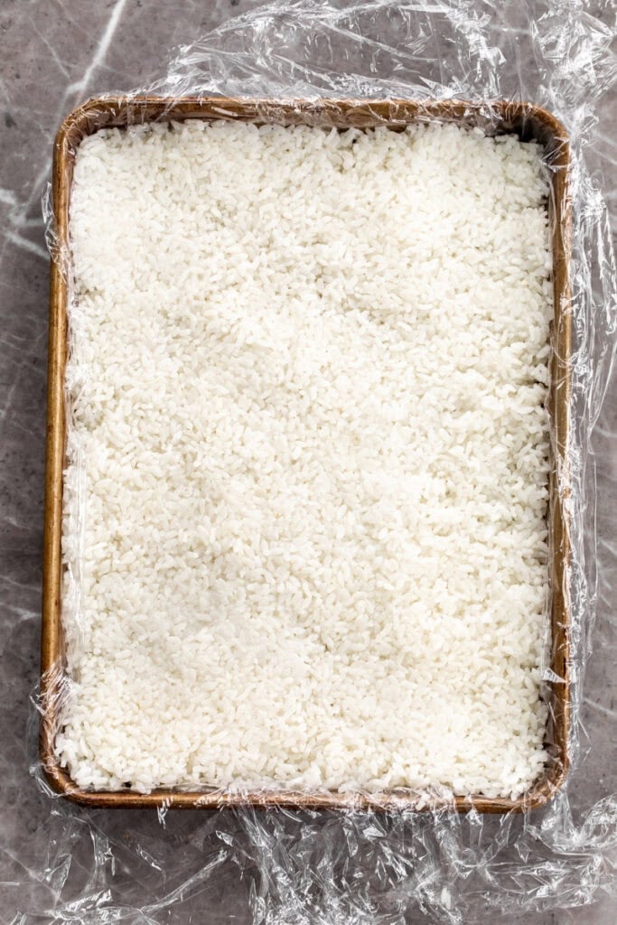 sushi rice on baking sheet lined with plastic wrap.
