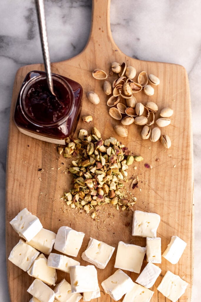 ingredients with jam and pistachio and brie on cutting board.