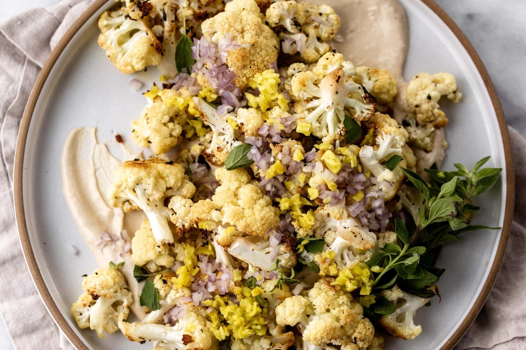Roasted Cauliflower with Tahini recipe topped with pepperoncini and shallots.