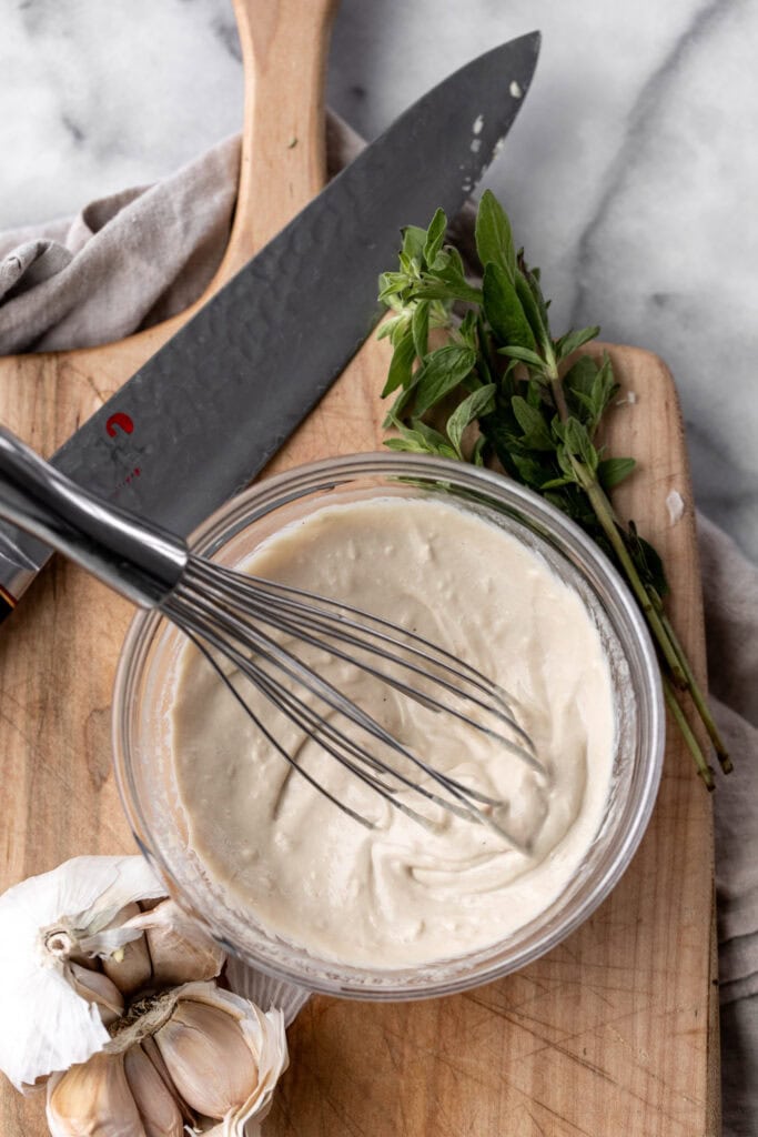 tahini sauce whisked in small mixing bowl on cutting board with knife.