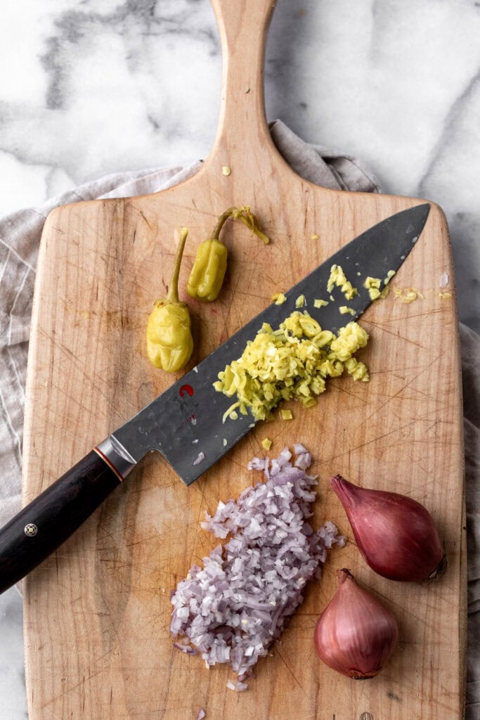 sliced pepperoncini peppers and shallots on cutting board.