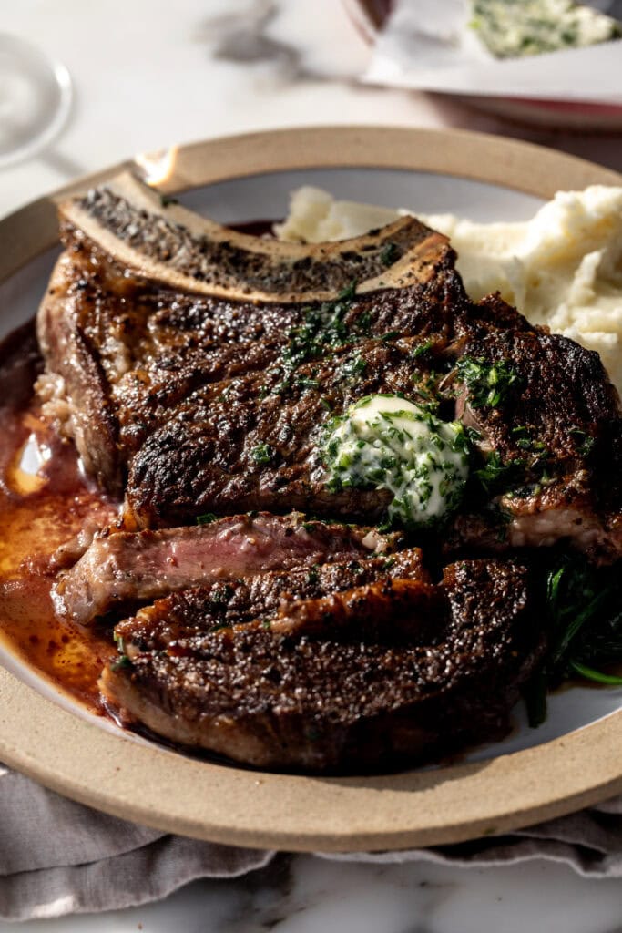 seared bone-in ribeye steak with garlic herb compound butter sliced.