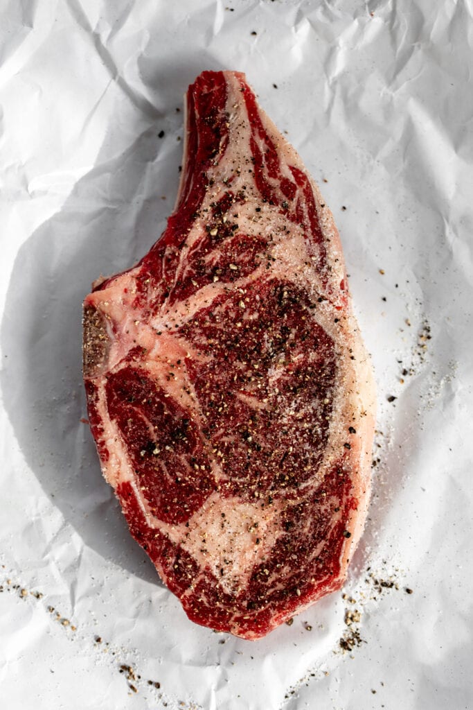 seasoned ribeye steak with salt and pepper on parchment paper.