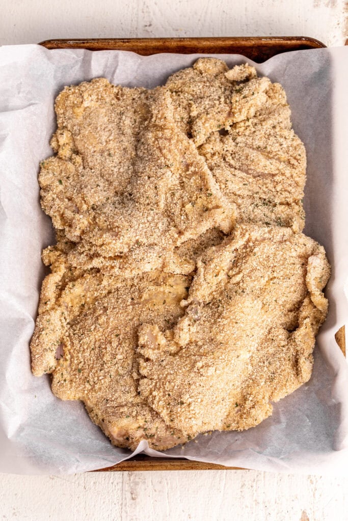 chilled dredged chicken on parchment paper lined baking sheet.