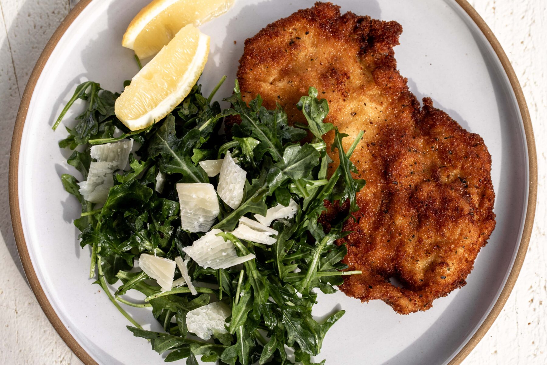 simple chicken milanese with arugula salad and lemon wedges on plate.