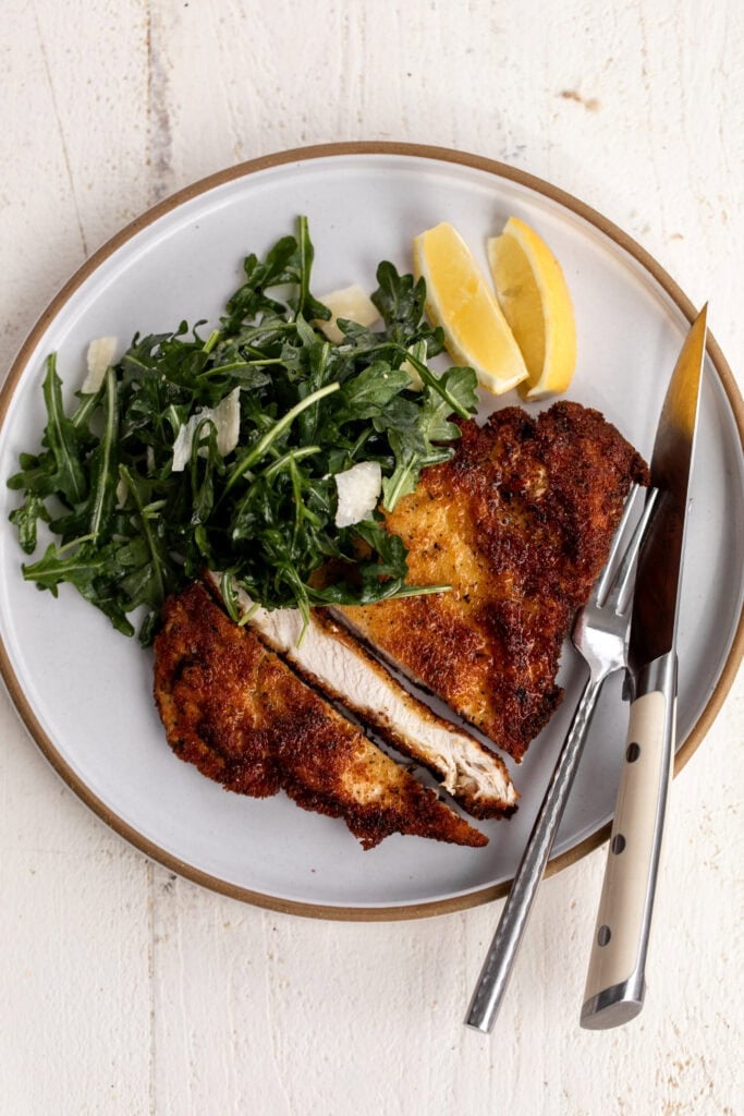 simple chicken milanese with arugula salad and lemon wedges cut into strips.