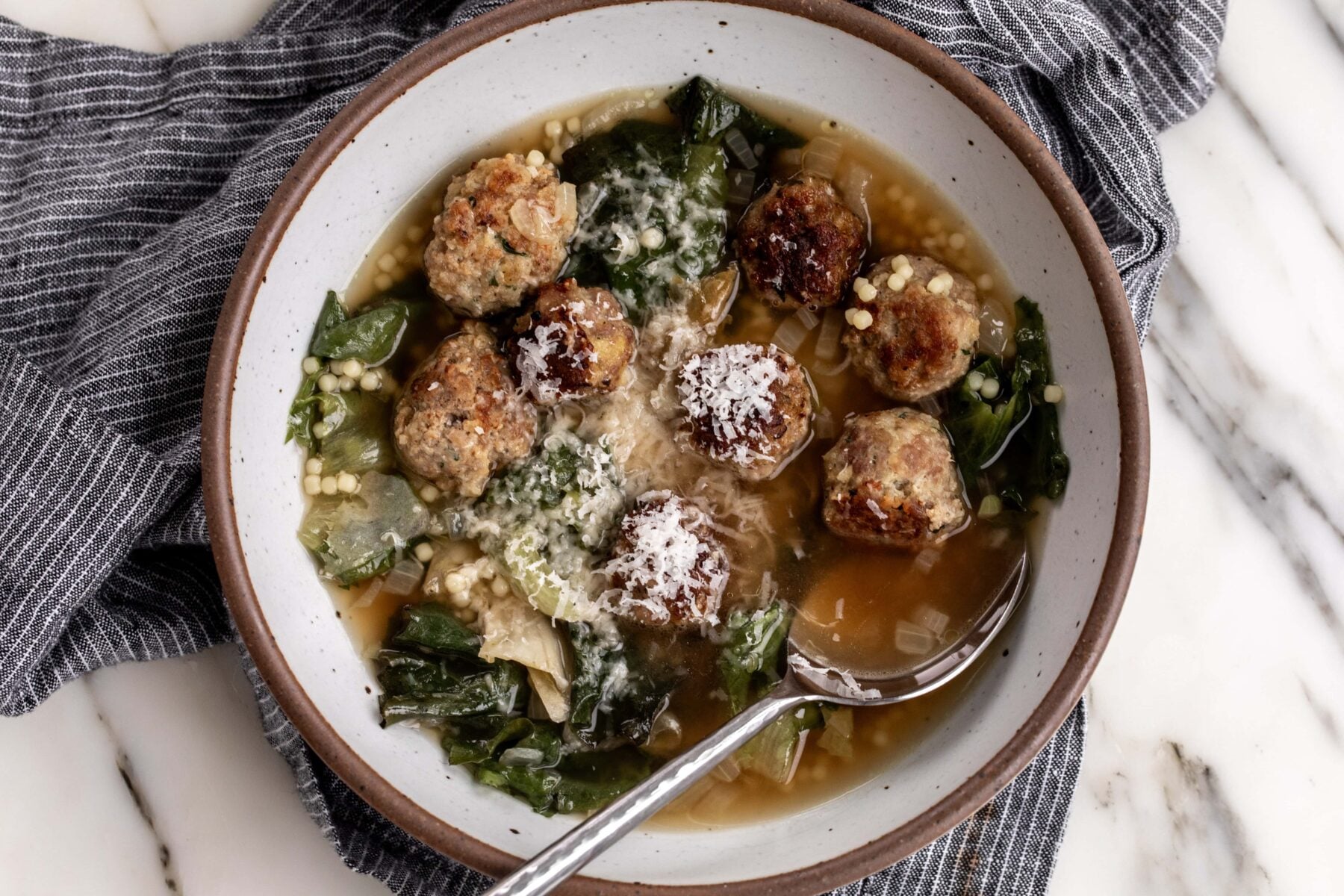 Italian wedding soup with chicken bone broth and escarole garnished with parmesan cheese.