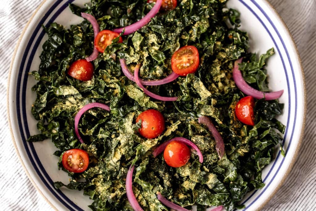 simple shredded kale salad with nutritional yeast with pickled red onion and cherry tomatoes.