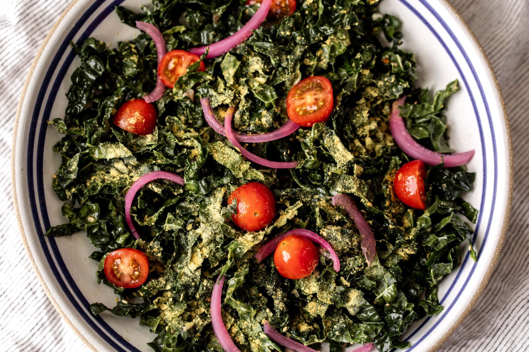 simple shredded kale salad with nutritional yeast with pickled red onion and cherry tomatoes.