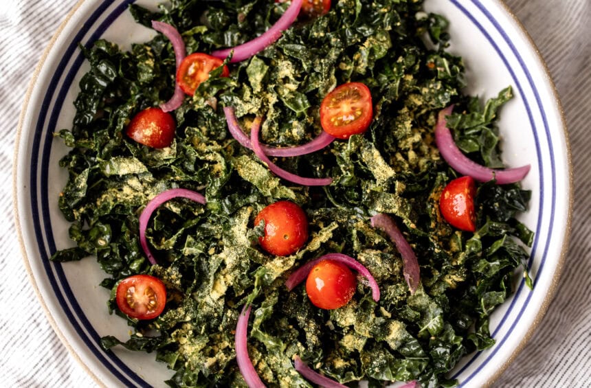 simple shredded kale salad with nutritional yeast with pickled red onion and cherry tomatoes.