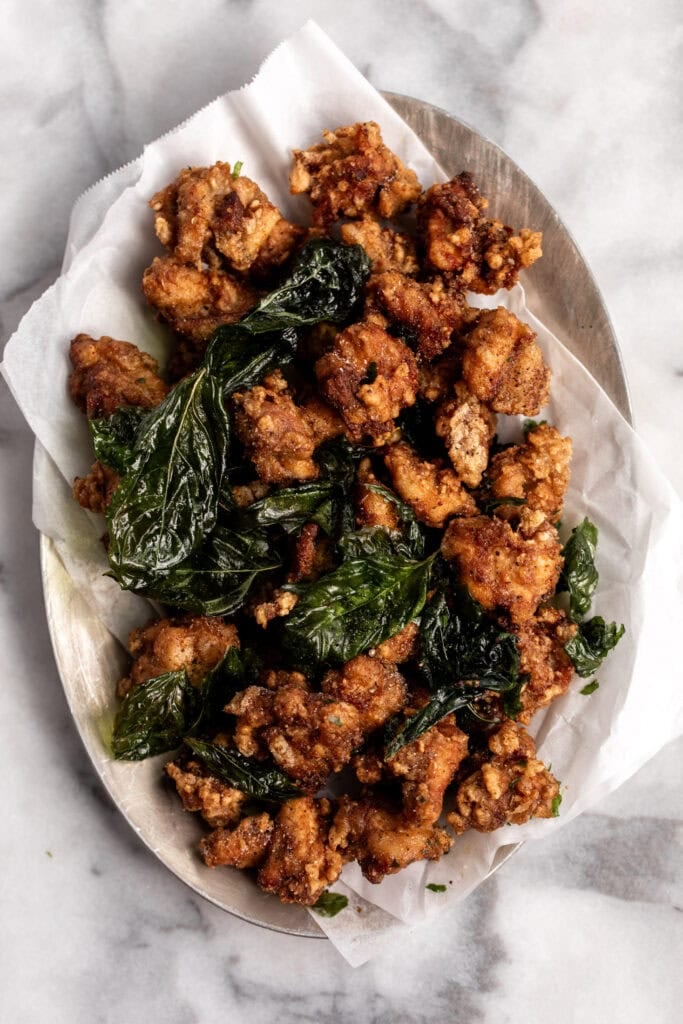 taiwanese popcorn chicken on silver platter with parchment paper and crispy basil leaves.