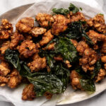 taiwanese popcorn chicken on silver platter with parchment paper and crispy basil leaves.