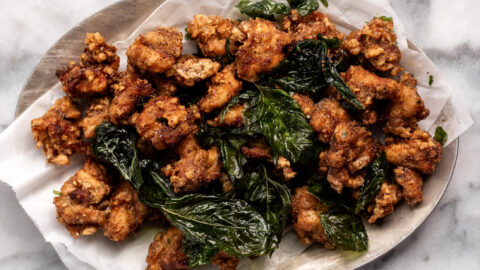 taiwanese popcorn chicken on silver platter with parchment paper and crispy basil leaves.