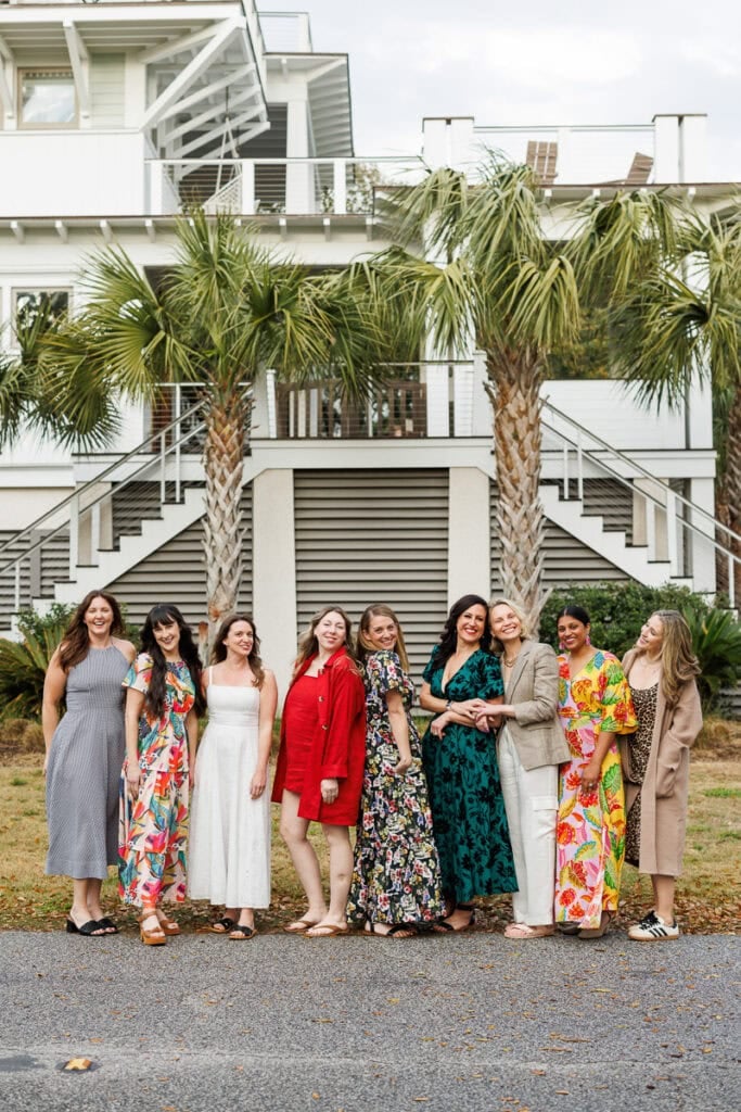 women standing outside house lined with palm trees.