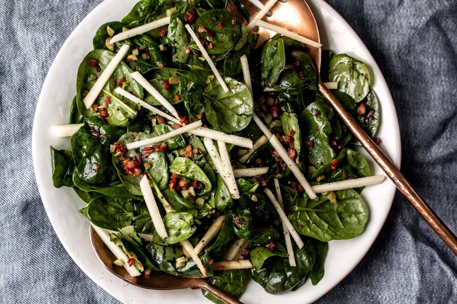 Warm Spinach Salad with copper serving spoons topped with pancetta and apples.