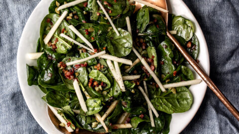 Warm Spinach Salad with copper serving spoons topped with pancetta and apples.