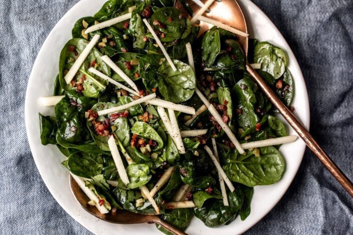 Warm Spinach Salad with copper serving spoons topped with pancetta and apples.