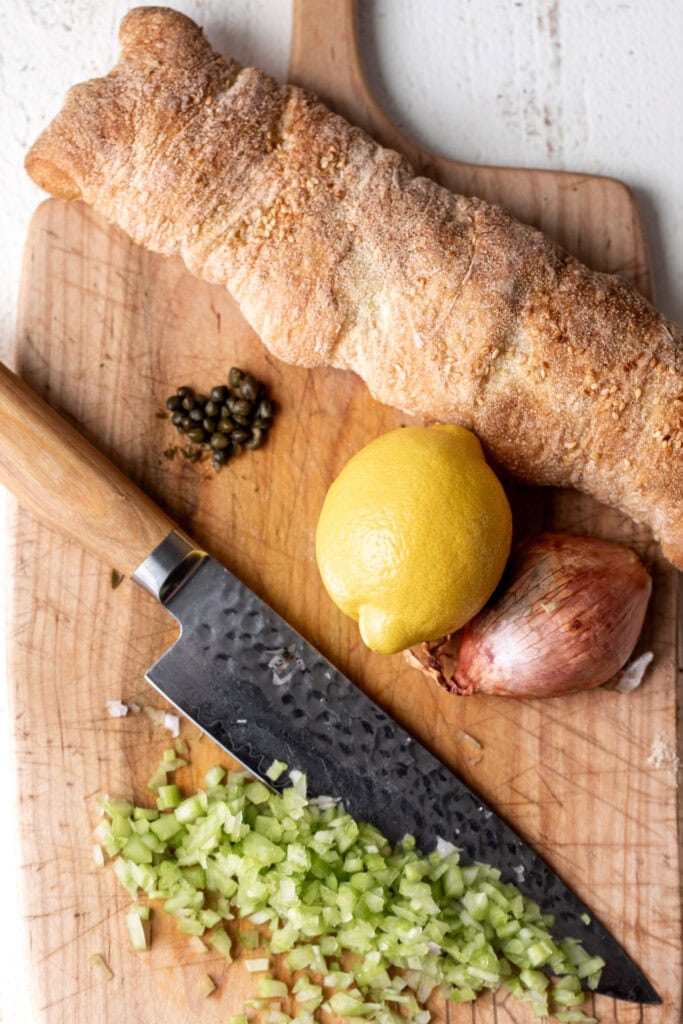 lemony tuna salad ingredients on cutting board with chopped celery, lemon, shallots, and capers.