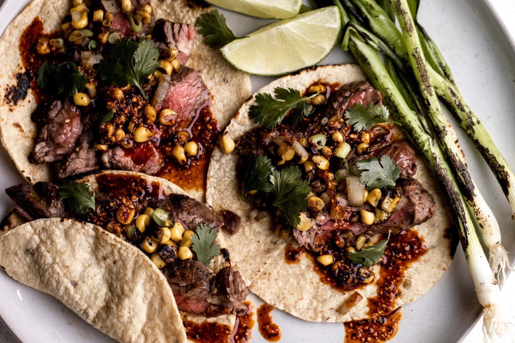 Seared steak tacos with salsa macha and charred corn with limes and green onion.