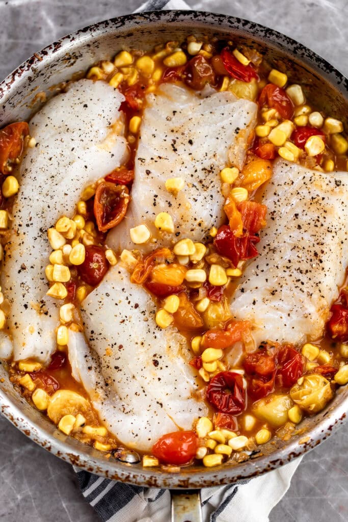 pieces of cod with tomatoes and corn in skillet.