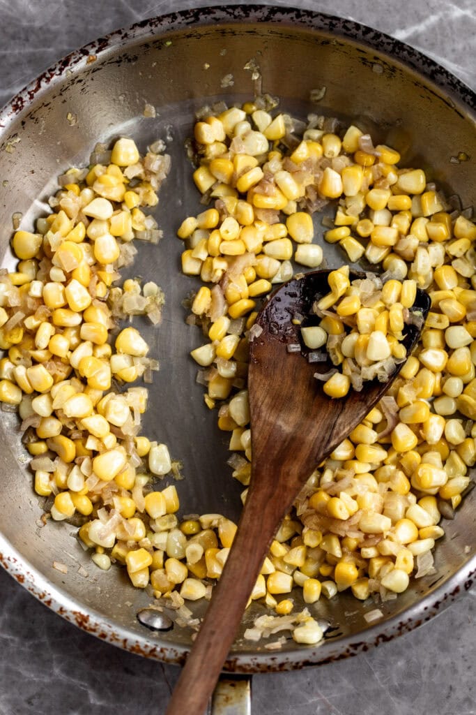 sauté pan with shallots and corn with wooden spoon.