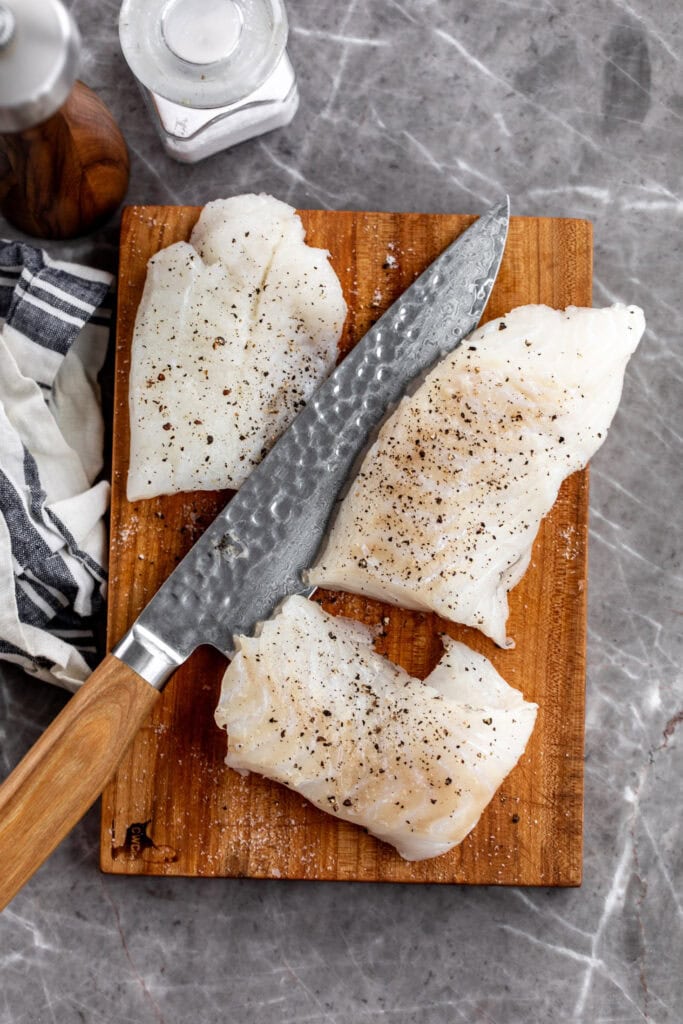 pieces of cod cut on cutting board seasoned with salt and pepper.