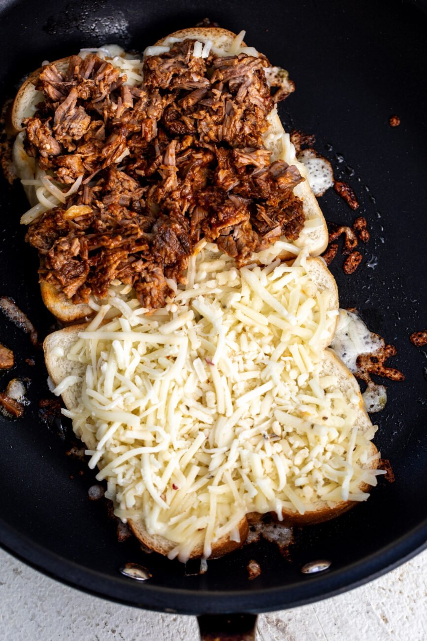 birria grilled cheese sandwich with shredded cheese in non-stick pan.