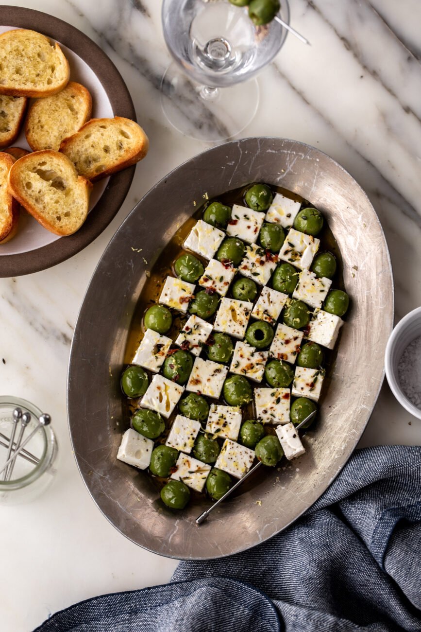 marinated olives and feta on serving platter with toothpicks and side of bread.