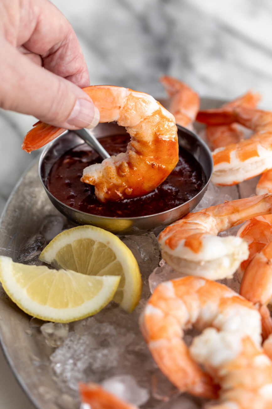 peeled and deveined shrimp dipped in cocktail sauce with lemon wedges.