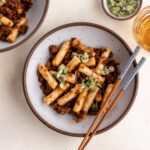 gochujang pork ragu with ginger scallion oil over rice cakes in bowl with chopsticks.