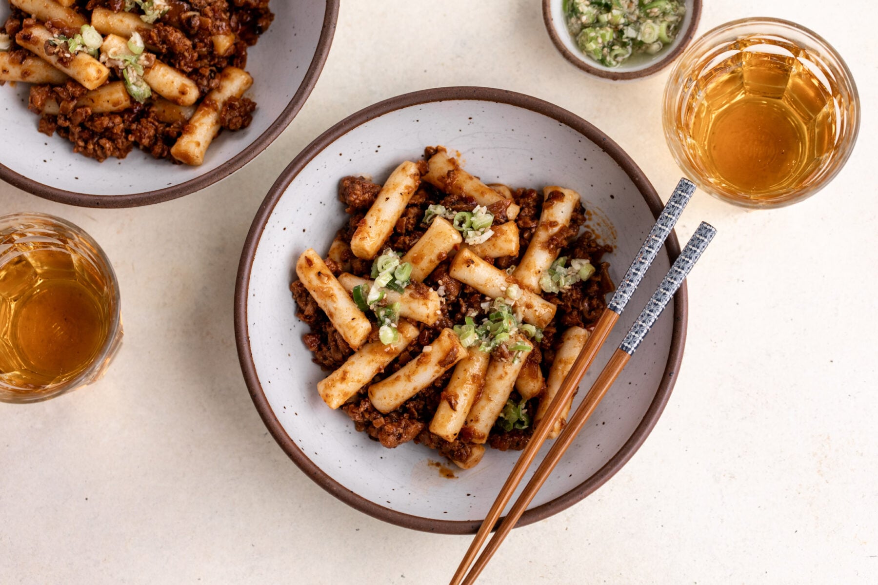 gochujang pork ragu with ginger scallion oil over rice cakes in bowl with chopsticks.