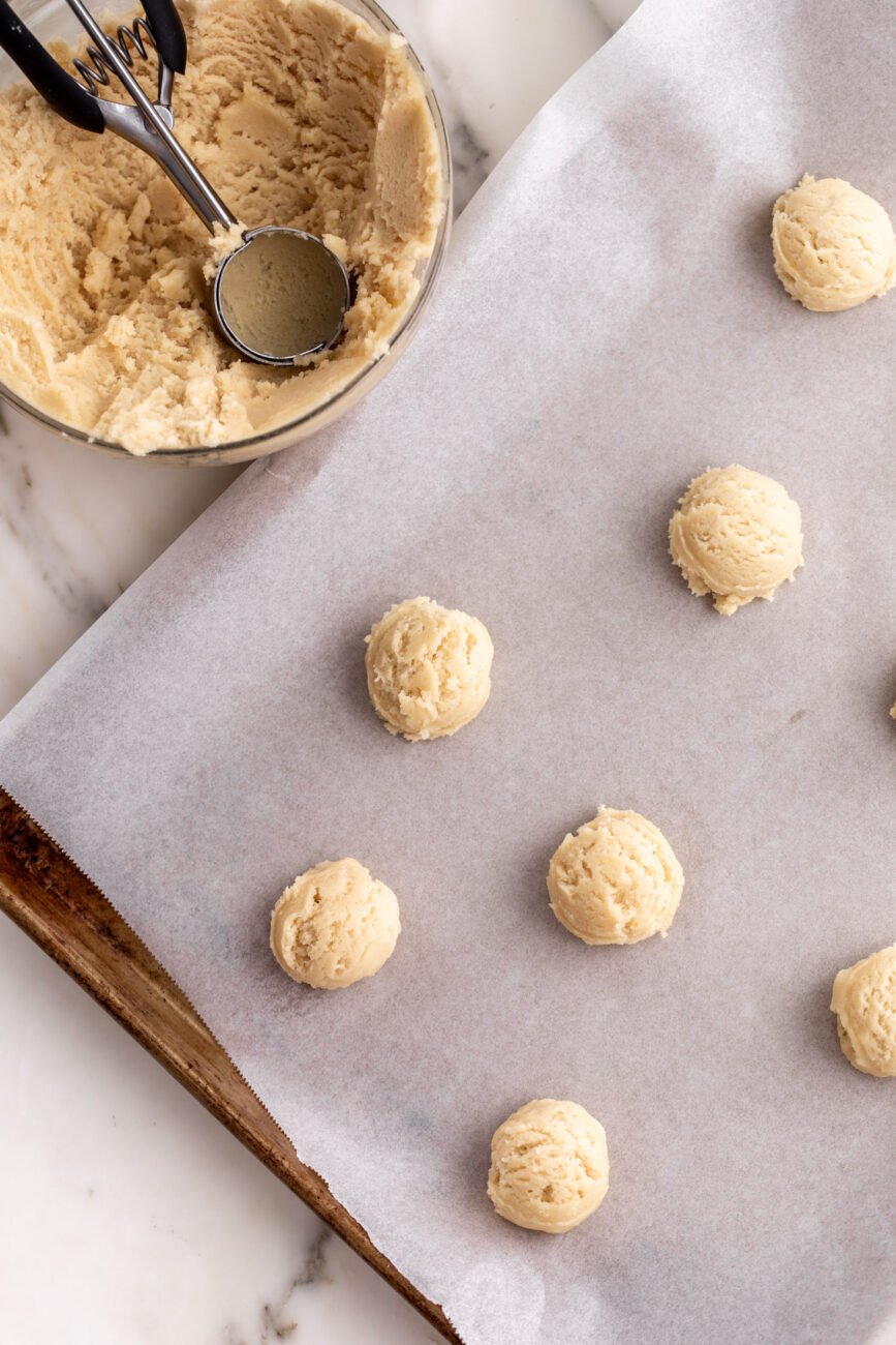 Scooped cookie dough balls on parchment paper lined baking sheet.