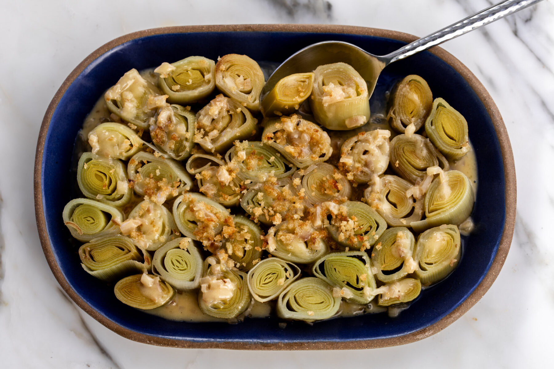 white wine-braised leeks with crispy buttered breadcrumbs with serving spoon.