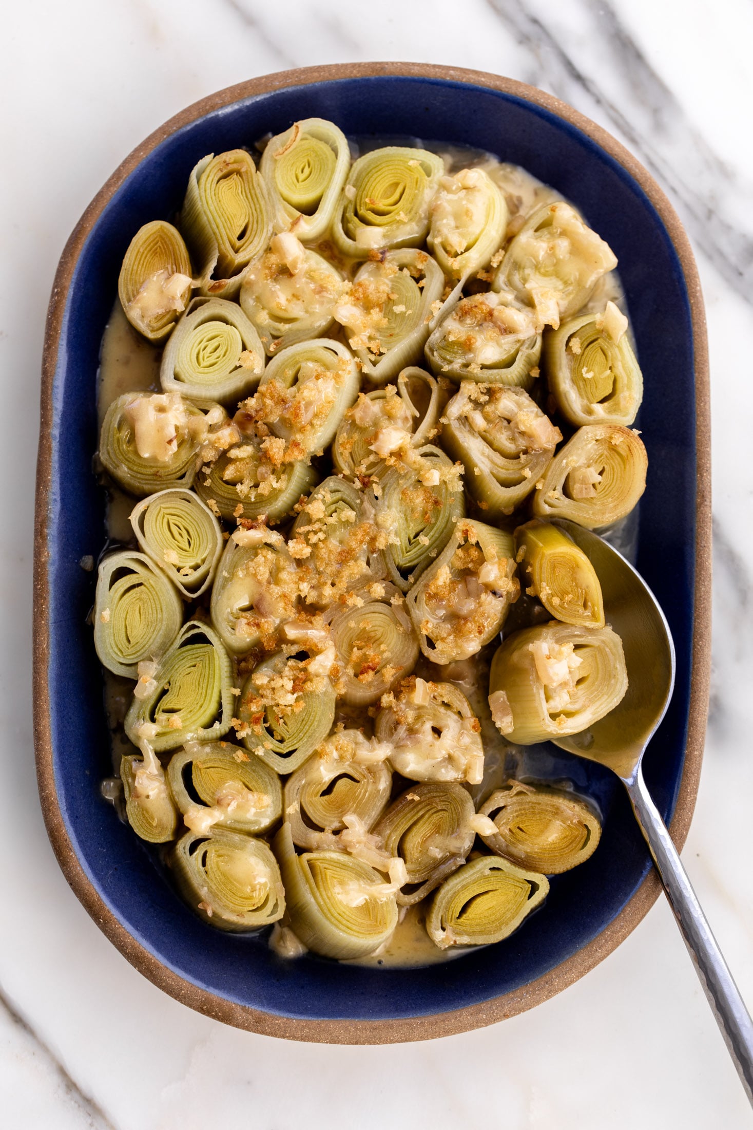 white wine-braised leeks with crispy buttered breadcrumbs with serving spoon.