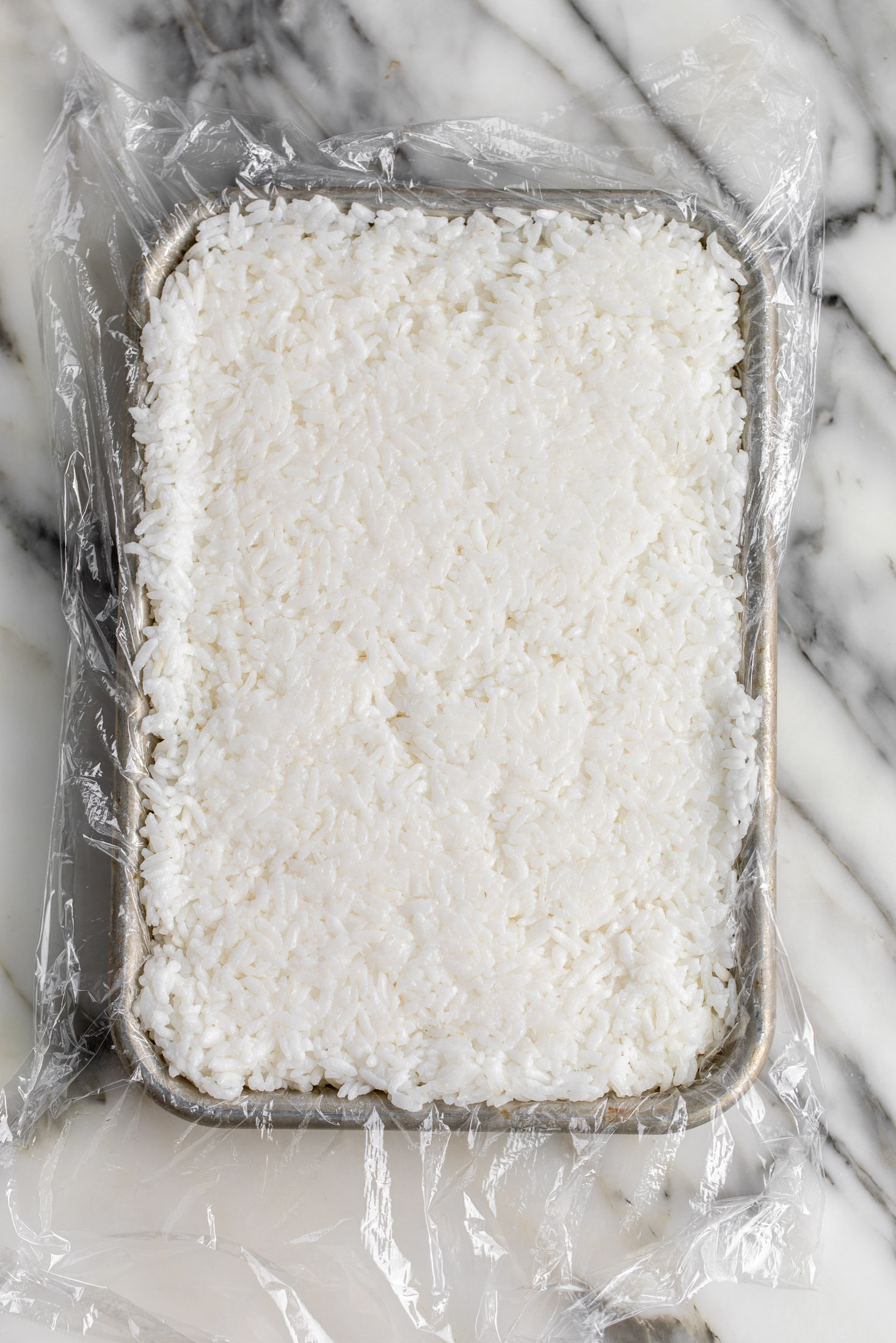 cooked sushi rice pressed into sheet pan with plastic wrap.