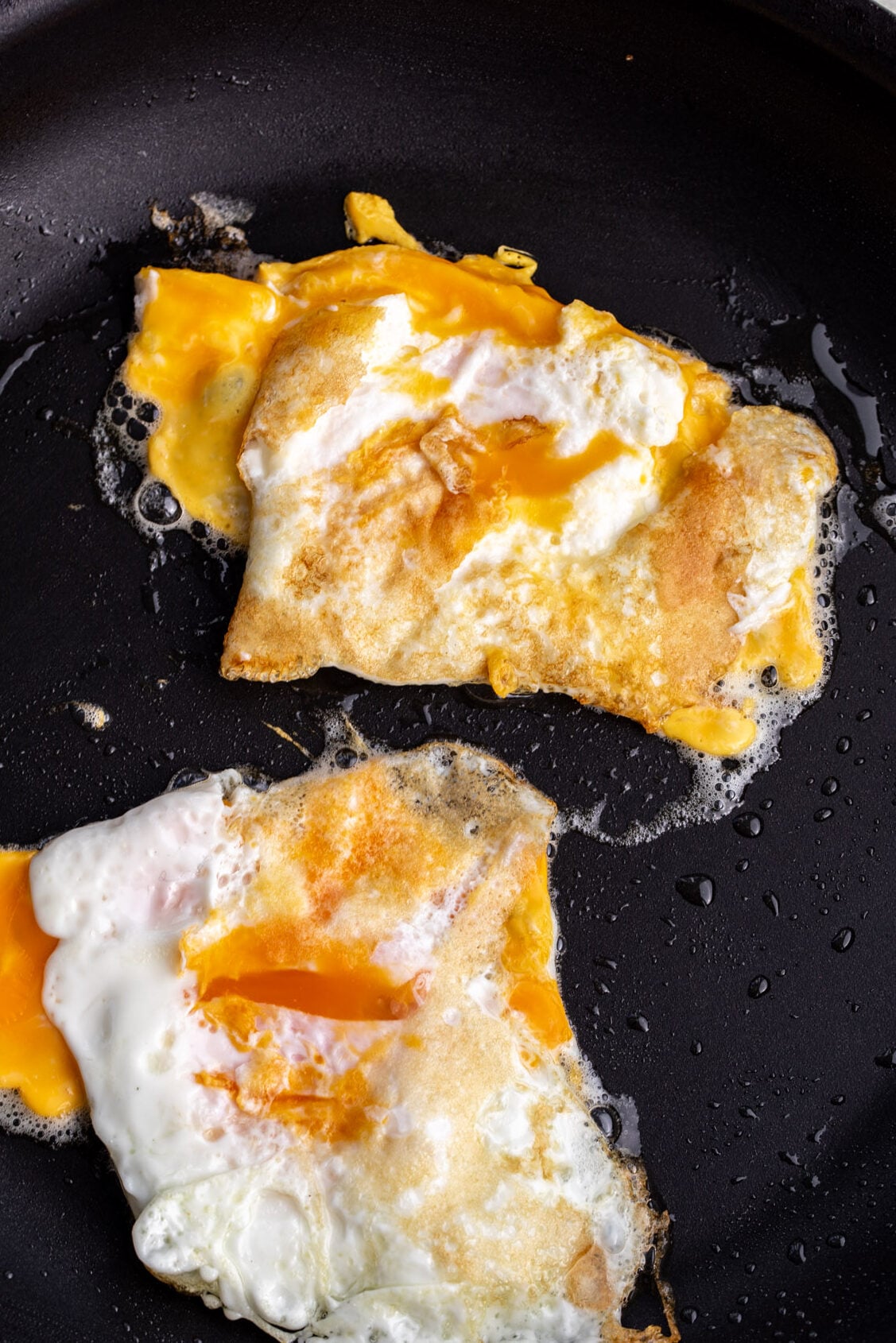 broken-yolk fried eggs in non-stick pan.