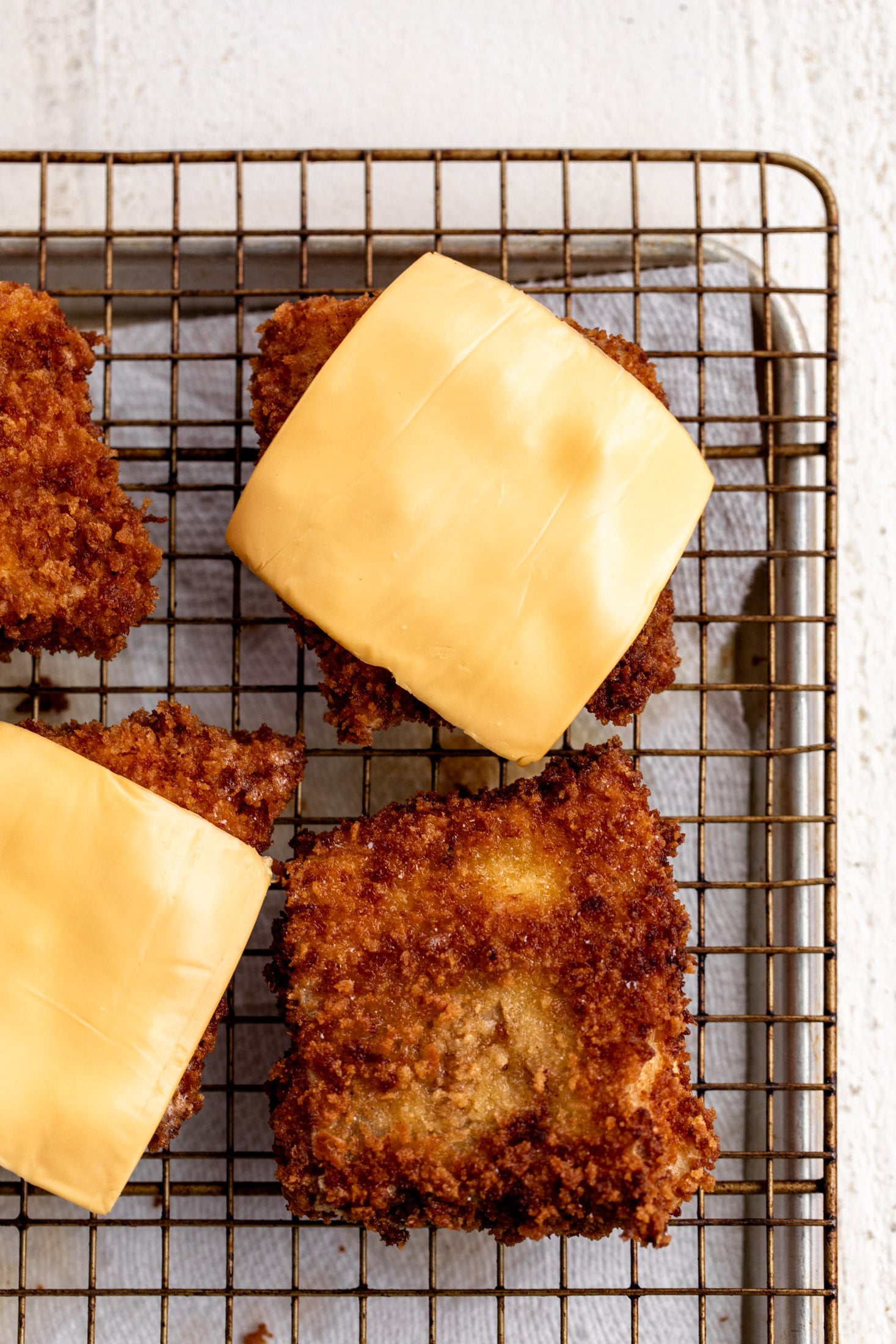 breaded fish with slices of American cheese on wire cooling rack.