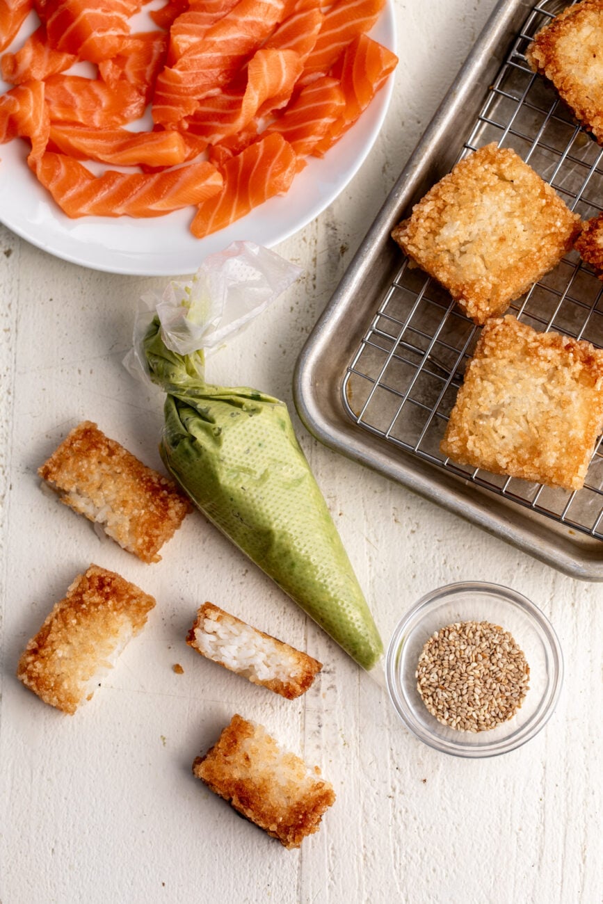 halved crispy rice pieces with avocado puree in piping bag and sliced salmon.