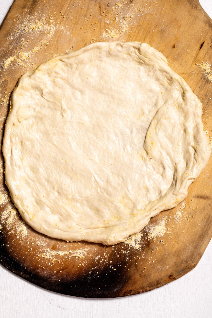 pressed and stretched out pizza dough on pizza peel.