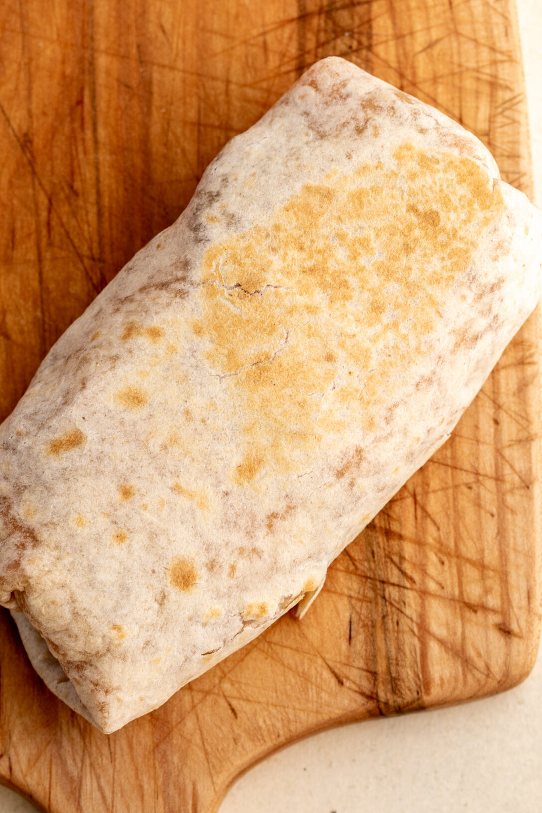 breakfast burrito with golden brown exterior on cutting board.