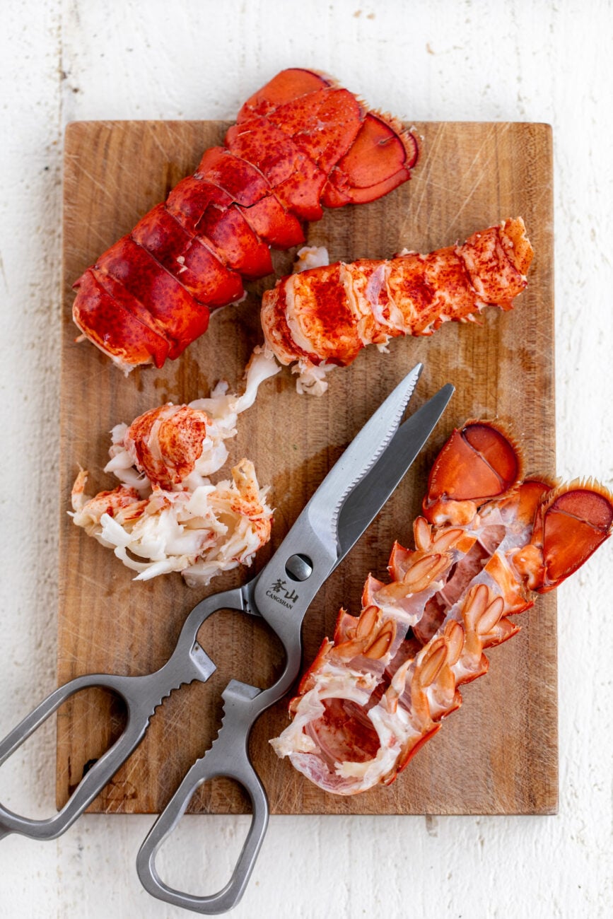 lobster tails cut with kitchen shears and shells removed on cutting board.