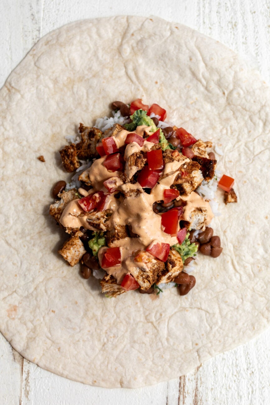 ingredients for burrito piled onto tortilla in layers.